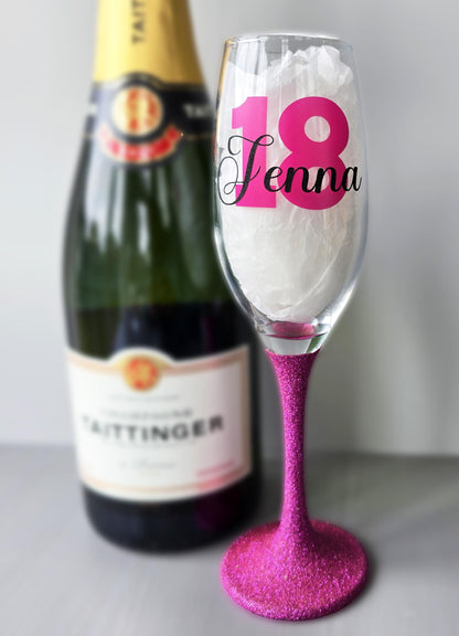 Personalised champagne flute or prosecco glass with glitter stem and with a birthday age number in block, glitter or metallic vinyl and a name in black decorative font through the number