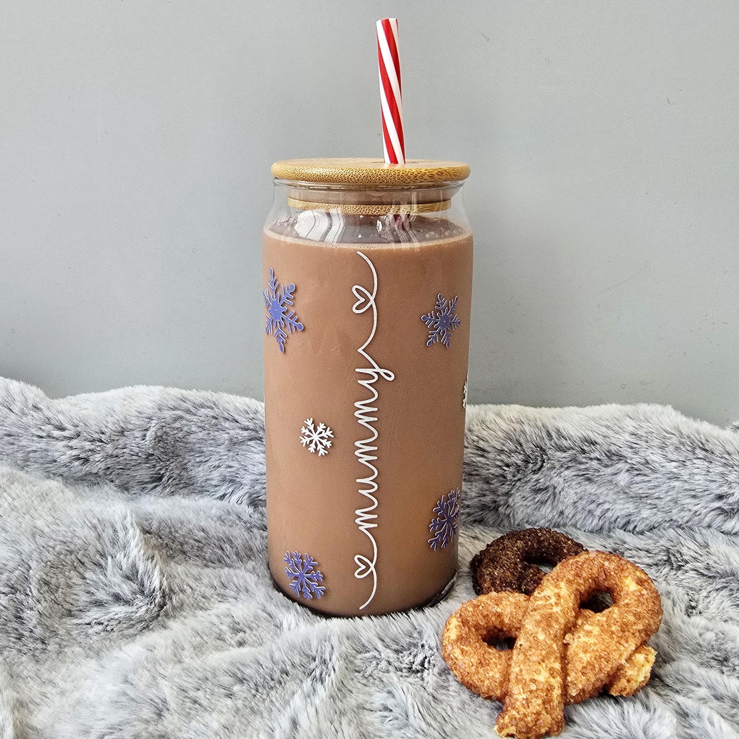 Personalised glass can drink holder with a bamboo suction lid and red and white reusable straw. Features silver snowflakes and blue snowflakes that colour change to purple when cold liquid is added to the glass. Personalised name along the side of the glass, available in glittery silver or black and features either a heart or stars at either end of the name.