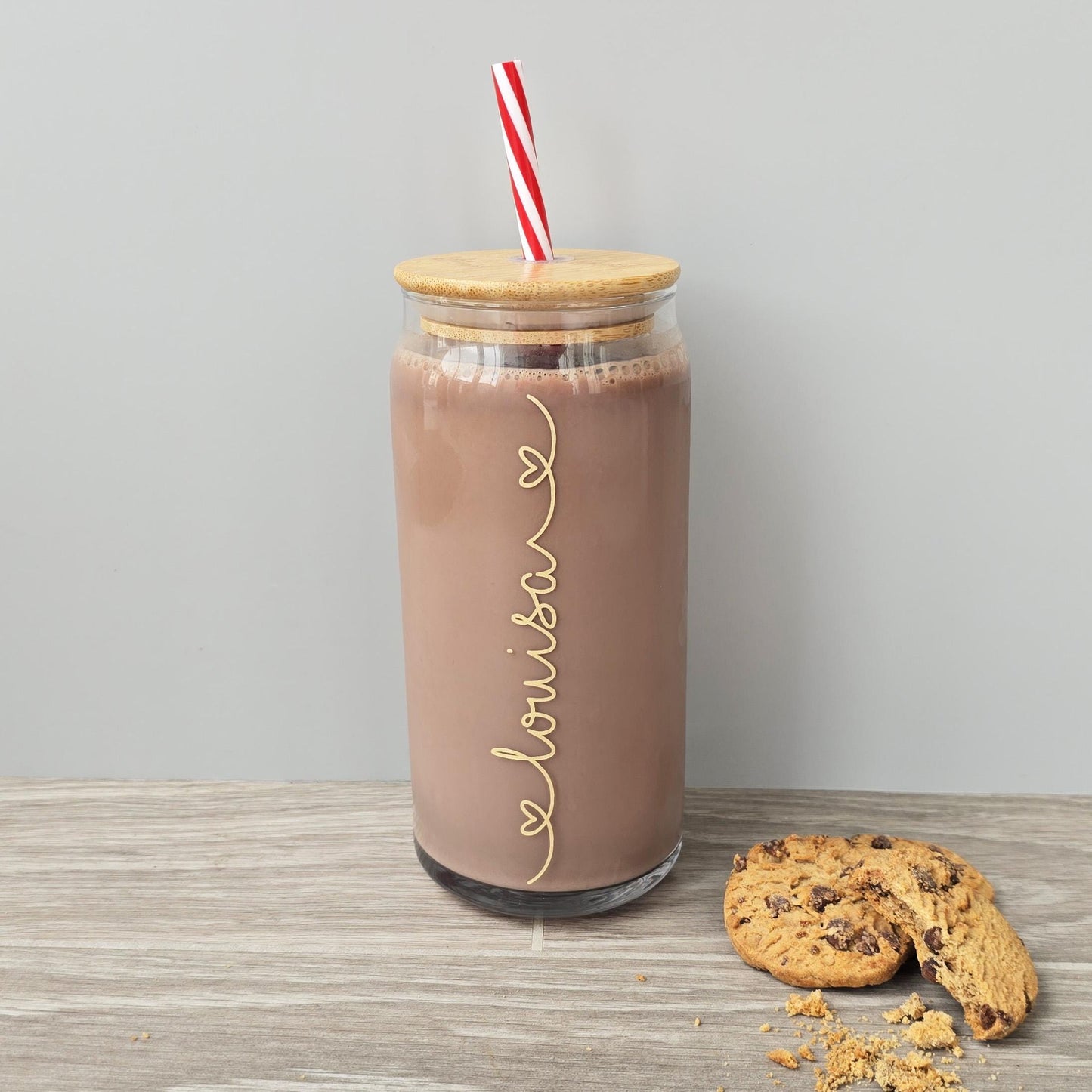 Personalised glass can drink tumbler with a bamboo suction lid and red and white reusable straw. Name printed in decorative font, in a range of colours, printed along the glass.