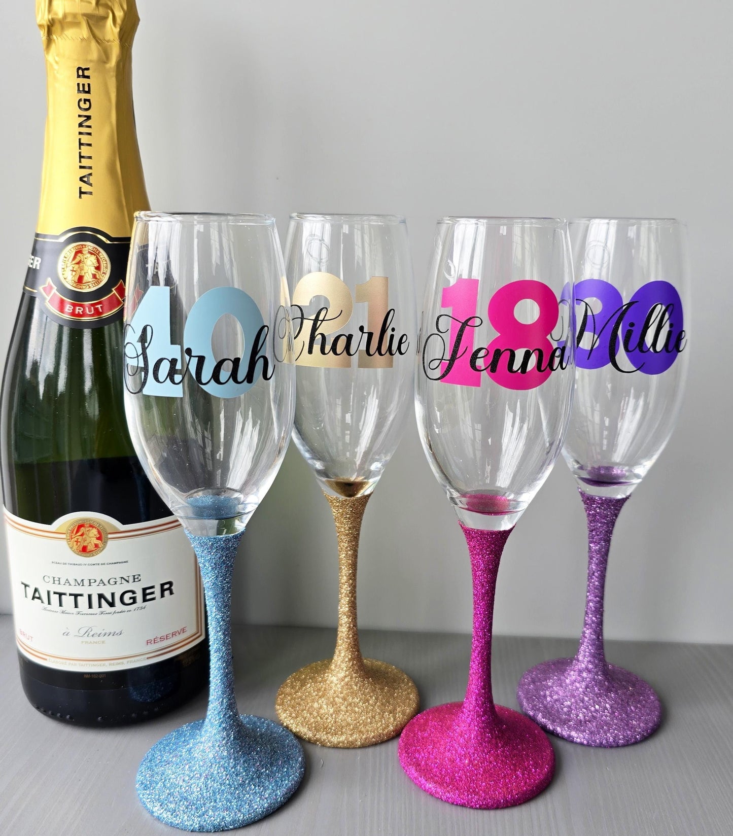 Personalised champagne flute or prosecco glass with glitter stem and with a birthday age number in block, glitter or metallic vinyl and a name in black decorative font through the number