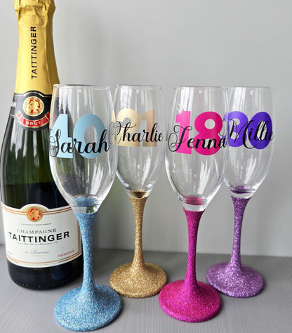 Personalised champagne flute or prosecco glass with glitter stem and with a birthday age number in block, glitter or metallic vinyl and a name in black decorative font through the number