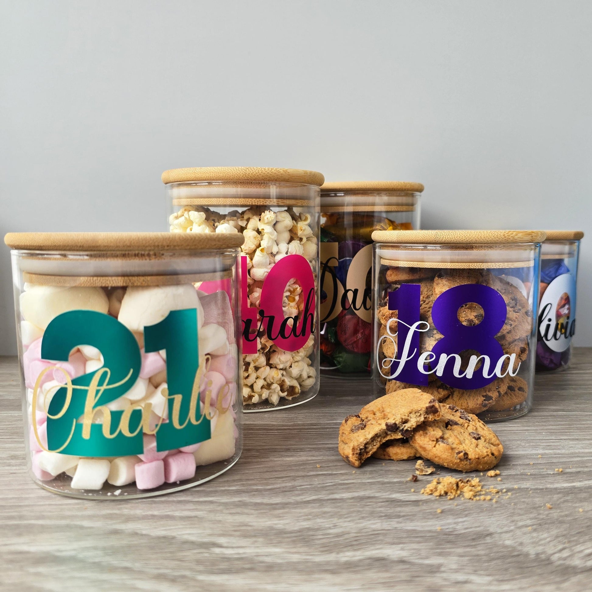 Decorative glass jars with personalized names and numbers on a wooden surface.
