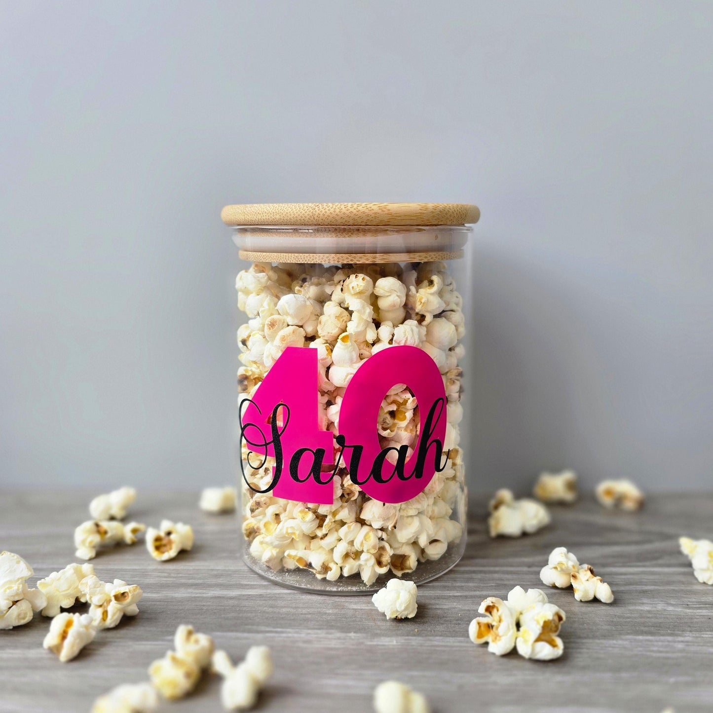 Glass jar filled with popcorn and personalized with '40 Sarah' on a wooden surface.
